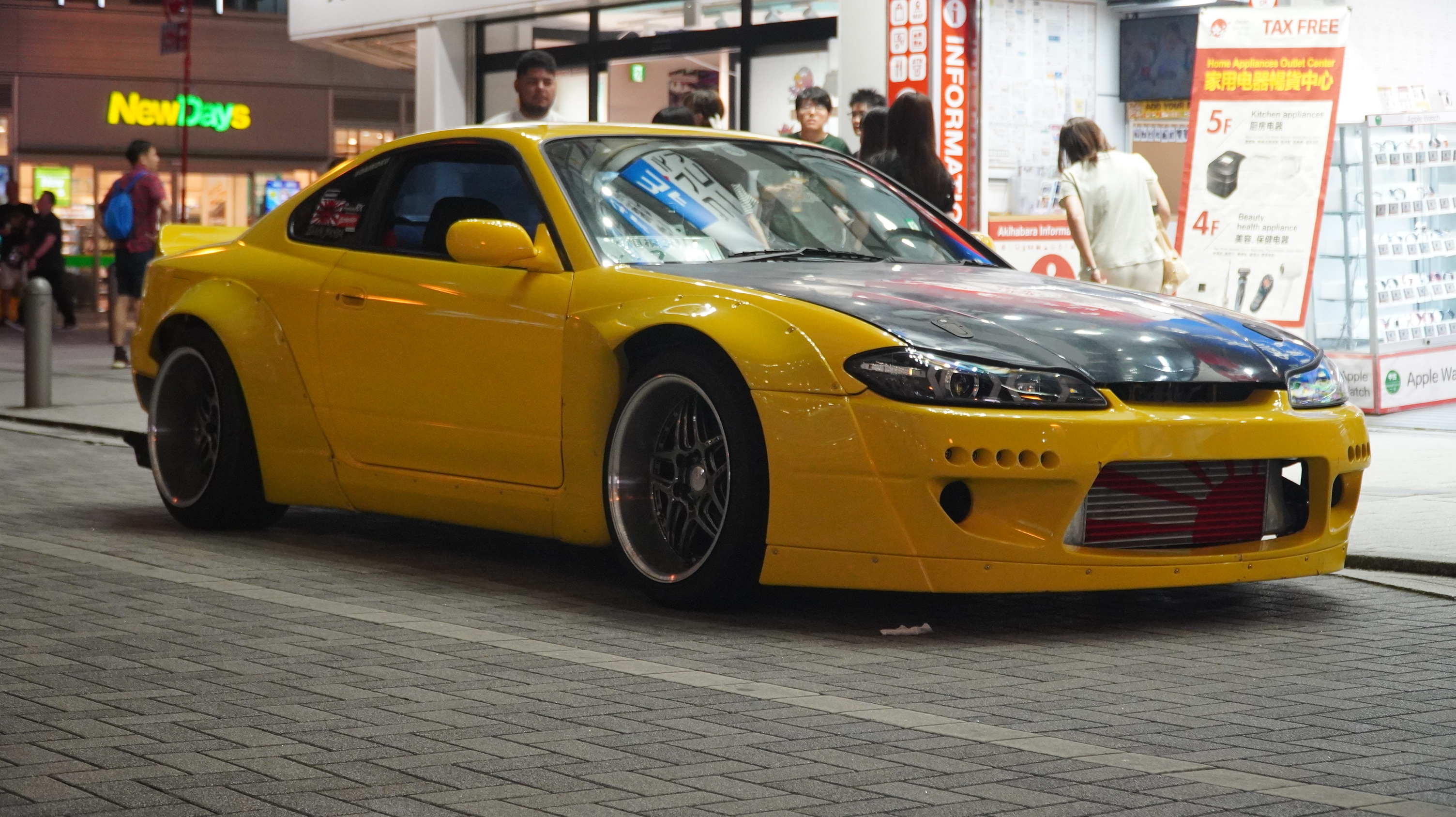 A modified yellow sports car parked on a Tokyo street at night